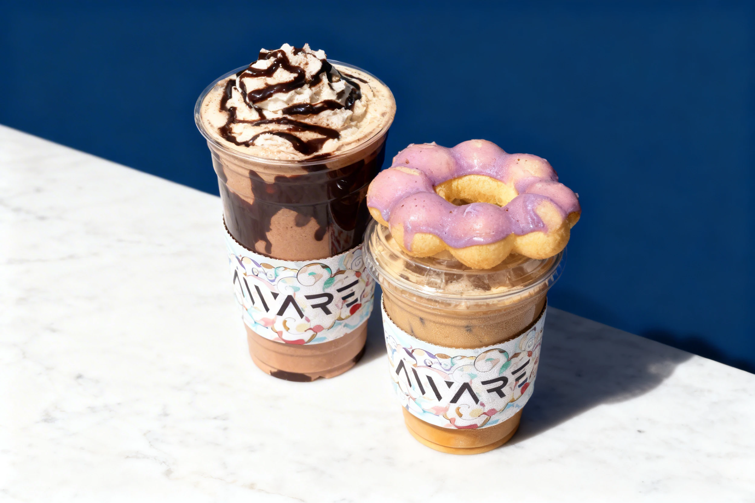 A chocolate frappe with chocolate drizzle and an iced coffee topped with a purple-glazed mochi donut.